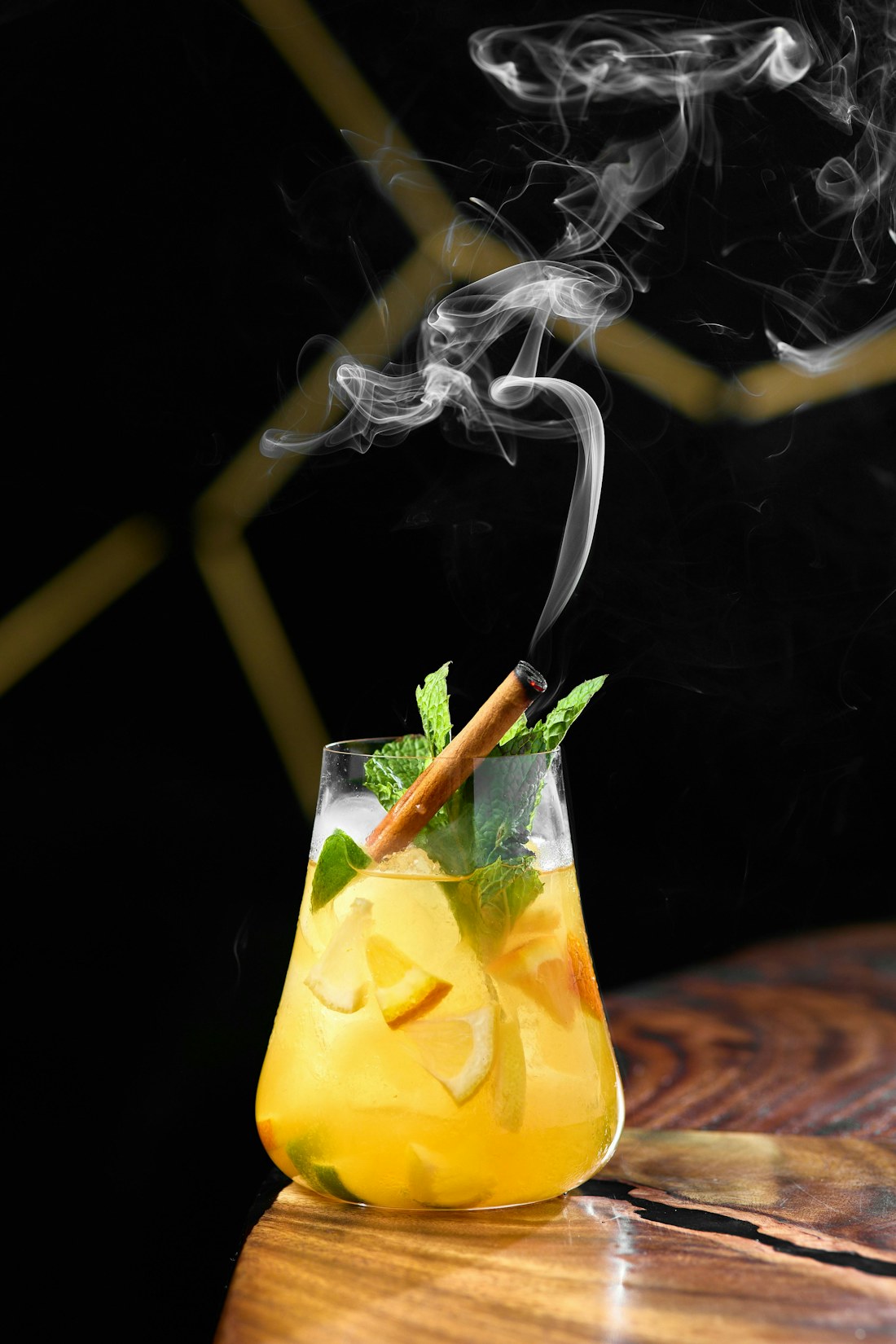 Cocktail con limone tagliato, menta e cannella fumante su fondo nero e oro
