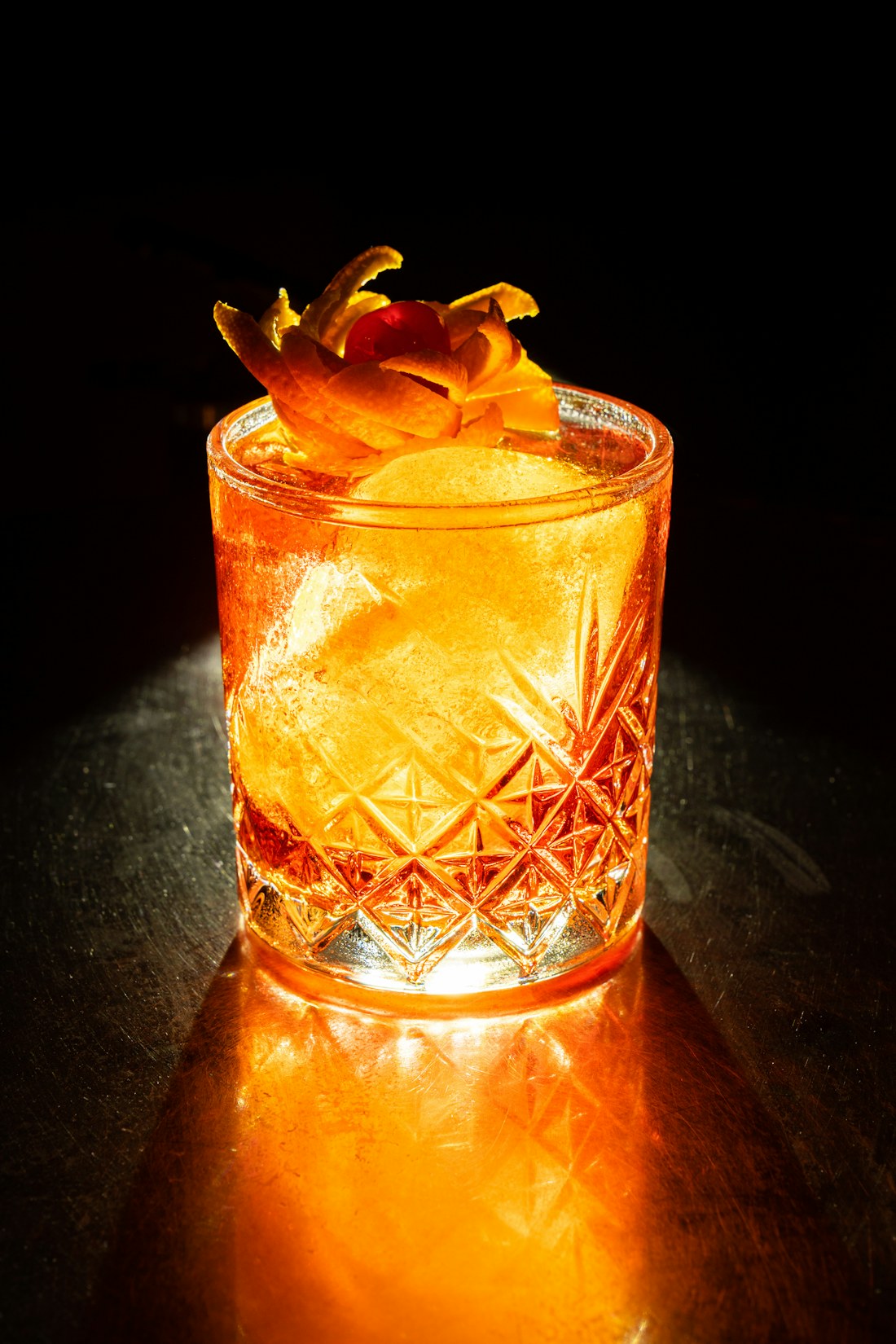 Cocktail su ghiaccio in bicchiere di cristallo intagliato, controluce ambrato