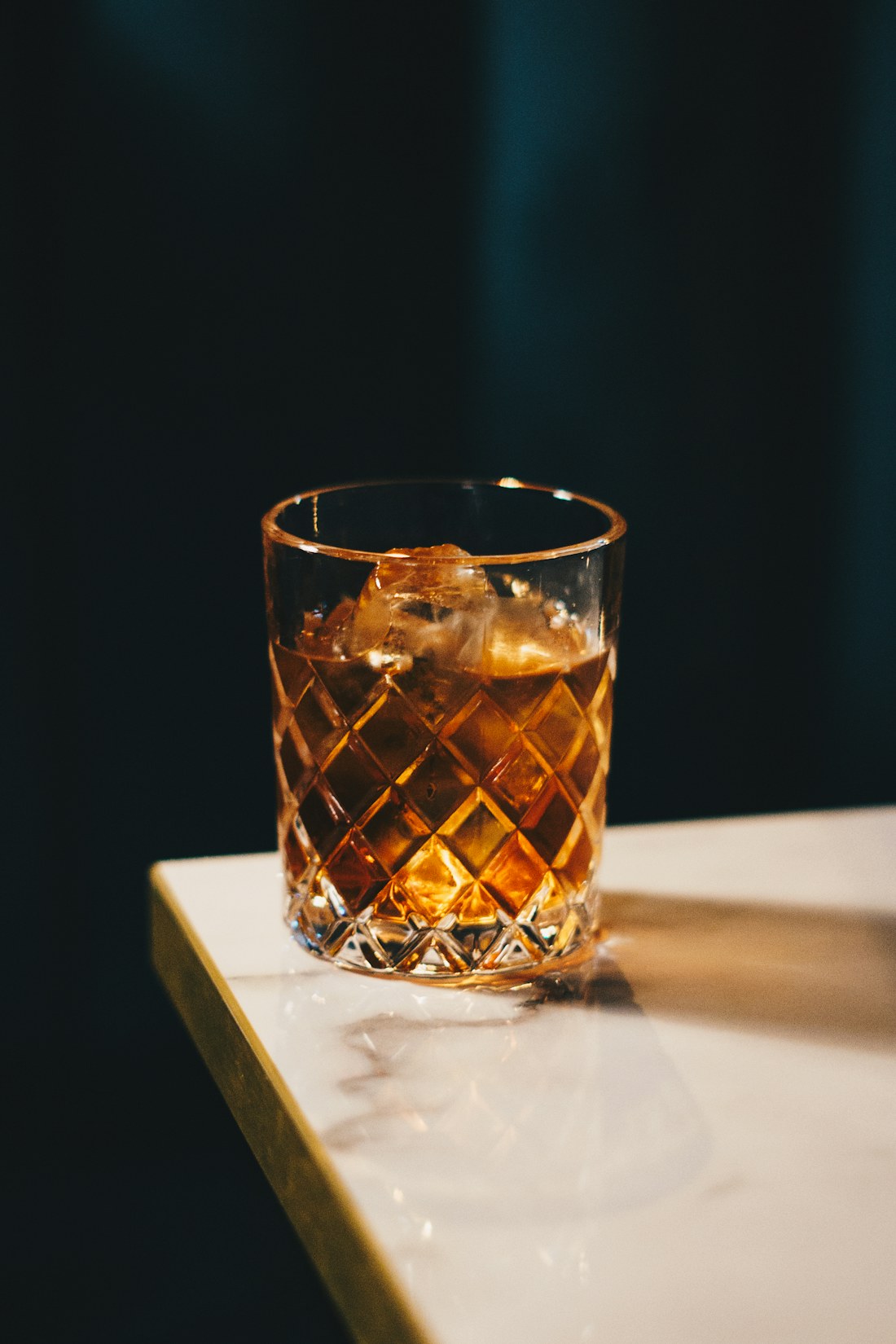 Bicchiere a rombi con distillato ambrato su marmo, fondo ottanio