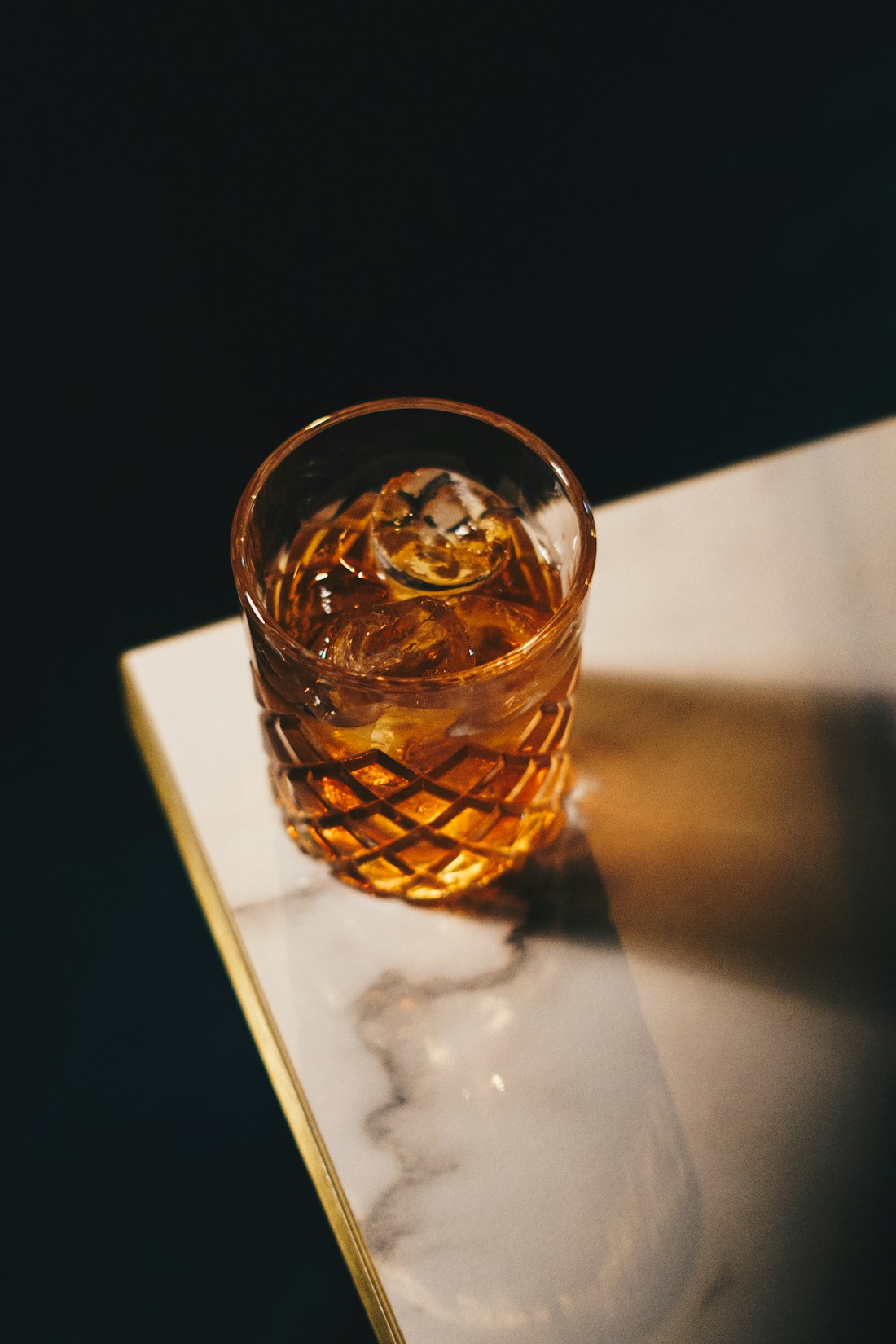 Bicchiere di cristallo intagliato con whisky e ghiaccio sull'angolo di un tavolo di marmo